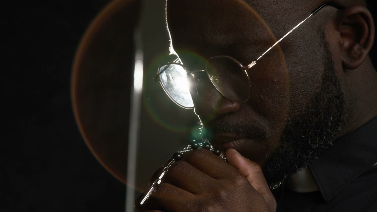Priest Praying with Rosary in Dramatic Light