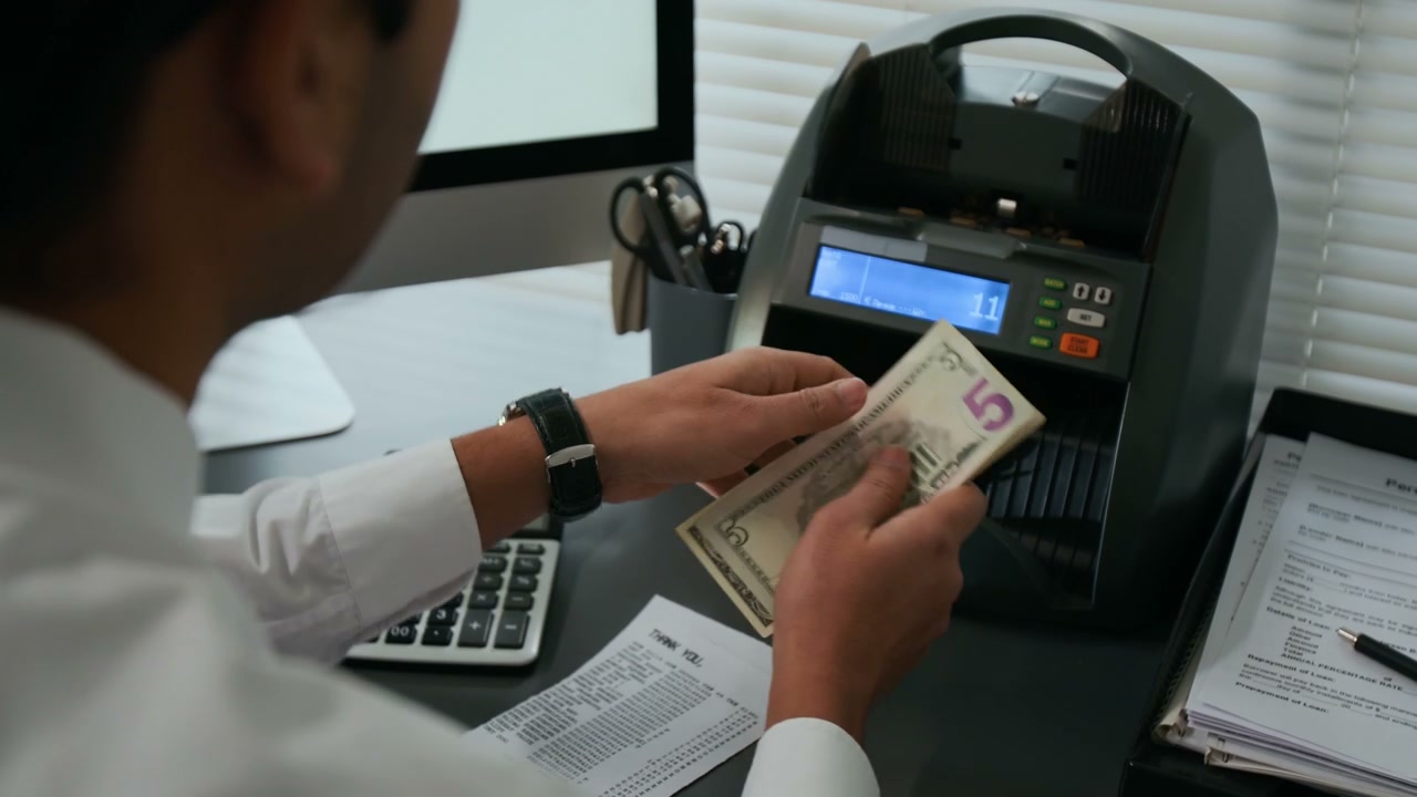 Close-up of Unrecognizable Employee Using Money Counting Machine in Bank Office