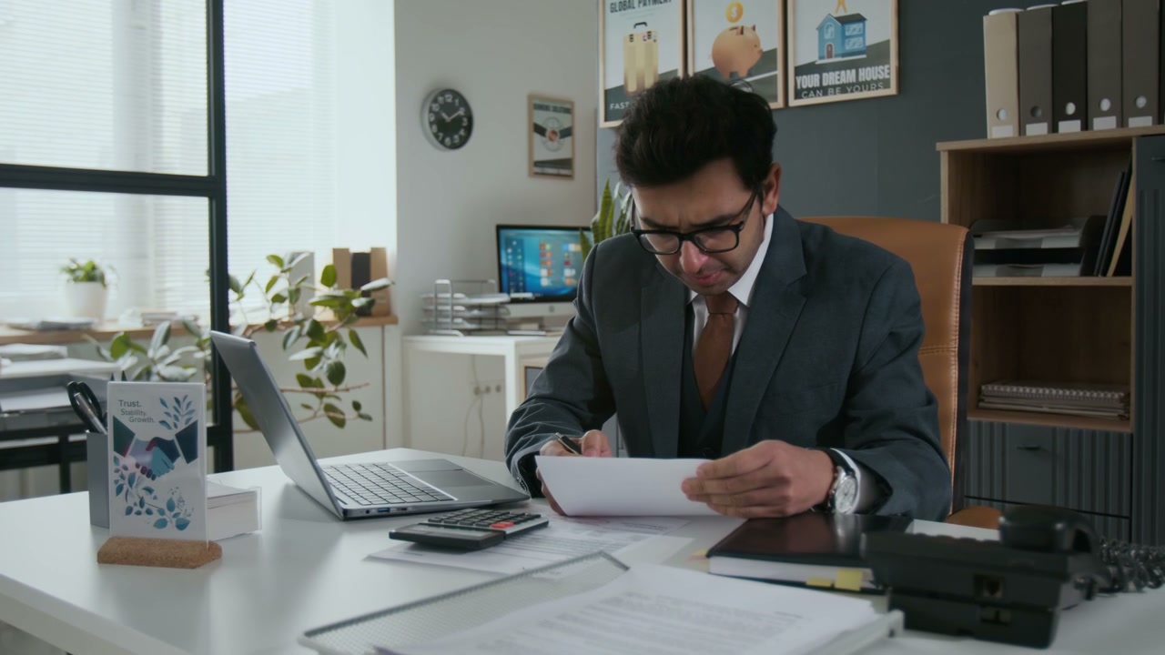 Businessman Reviewing Documents and Working on Laptop