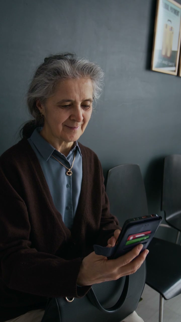 Senior Woman Using Smartphone While Waiting in Queue in Bank Office