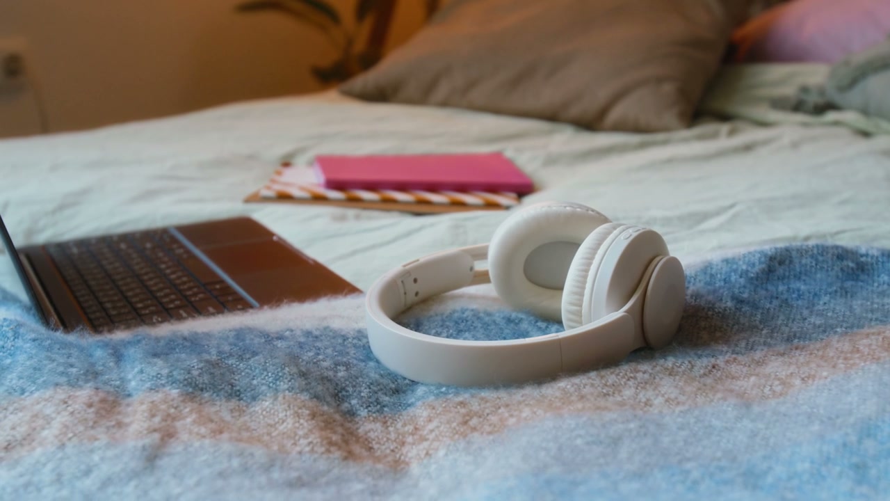 White Headphones and Laptop on Cozy Bed