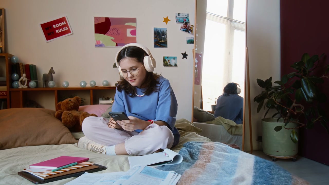 Young Woman With Headphones Using Phone in Bedroom