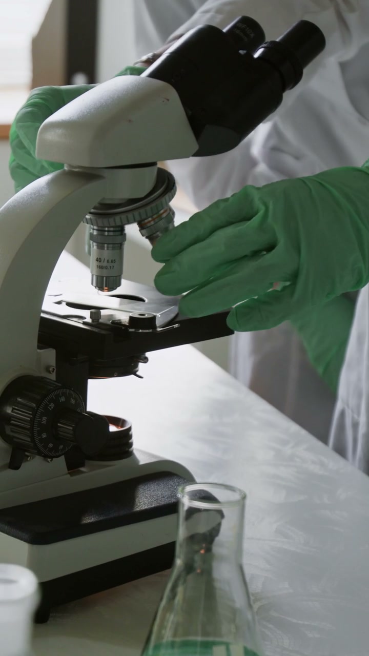 Person Adjusting Microscope in Laboratory