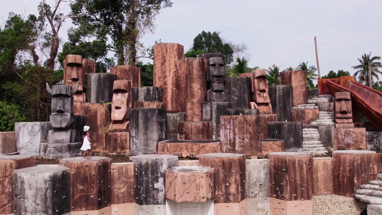 Woman Walks Through Tropical Stone Head Statues