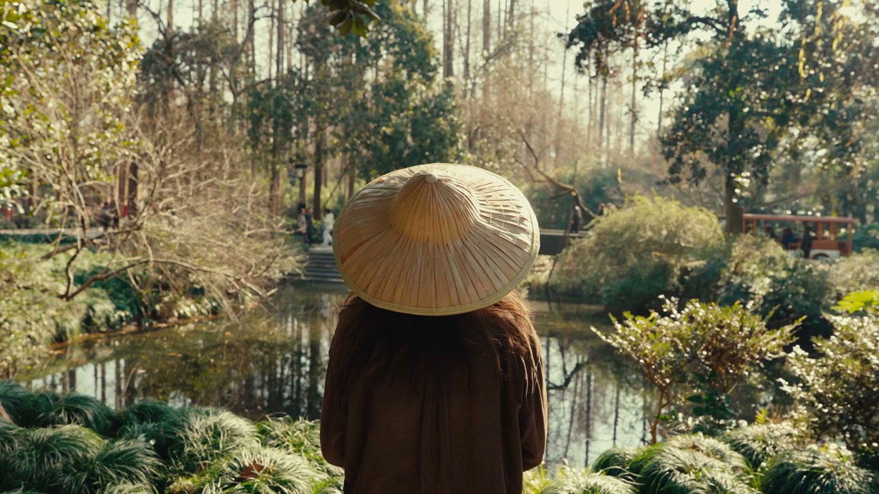 Person in Conical Hat Overlooking Garden Pond