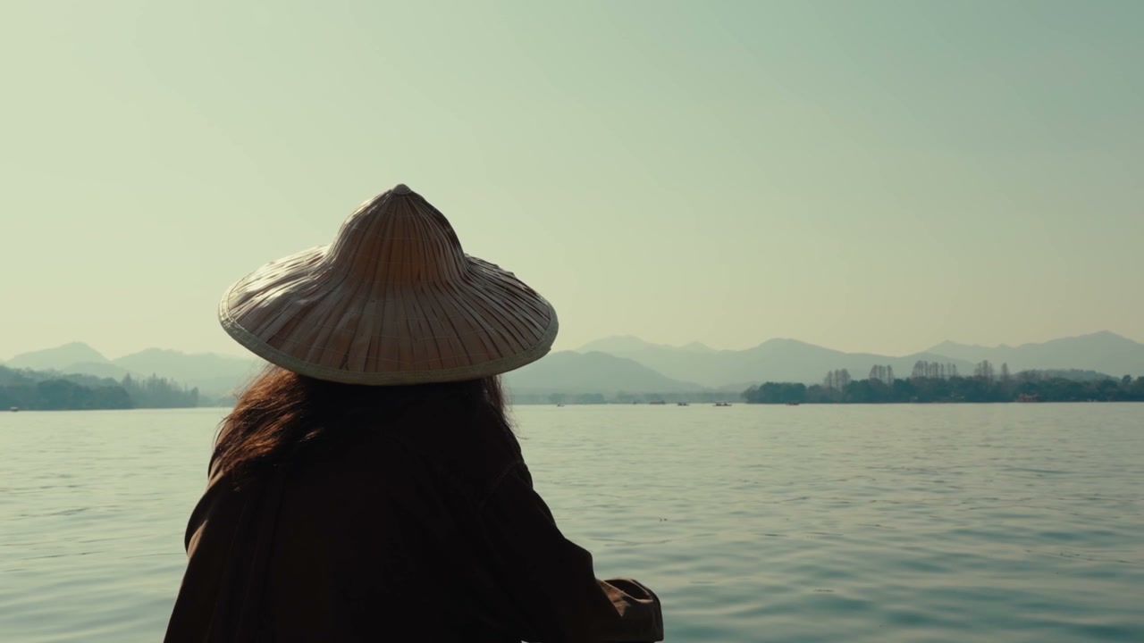 Person in Traditional Hat Boating on West Lake