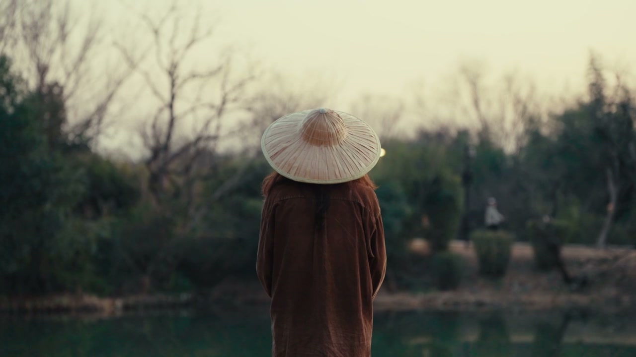 Person in Conical Hat Overlooking Park Pond