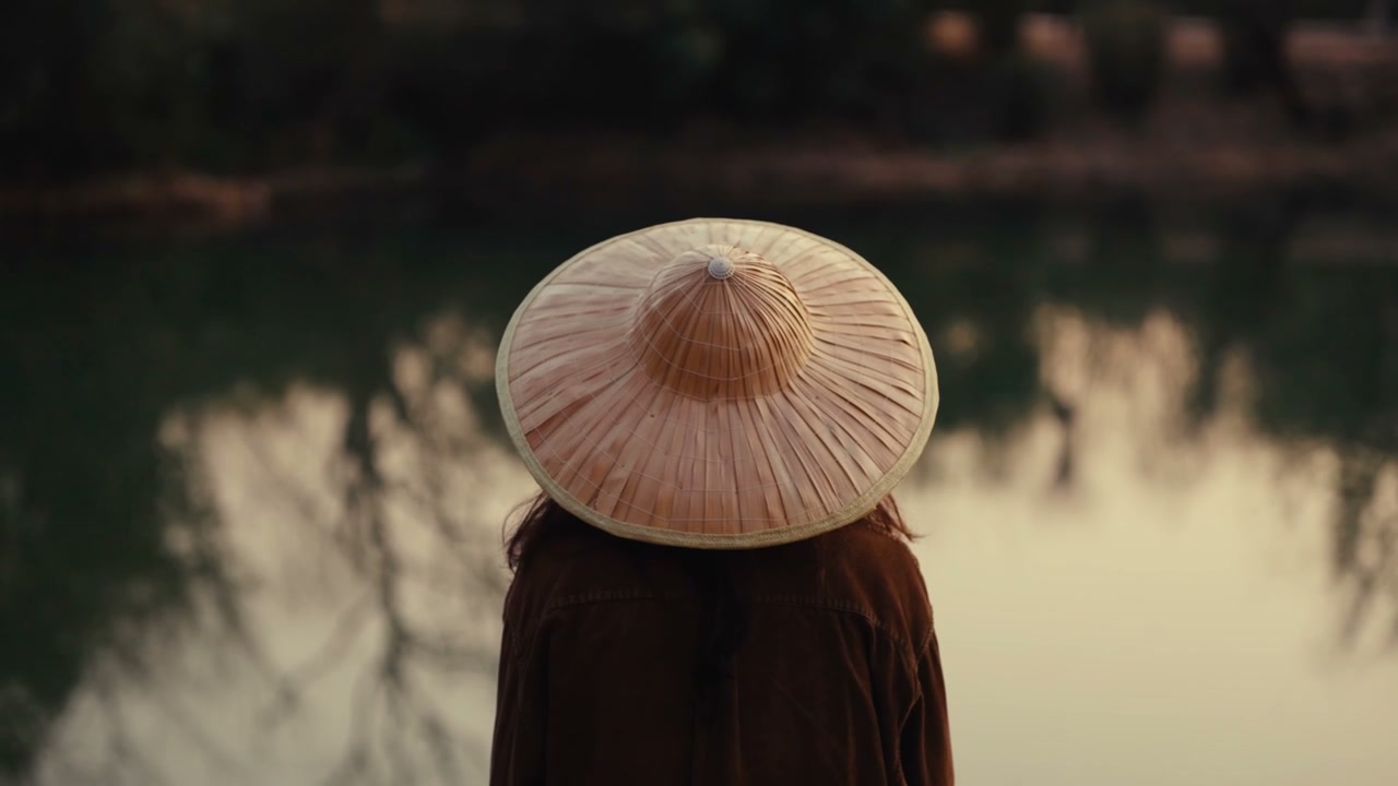 Person in Conical Hat Looking Over Lake