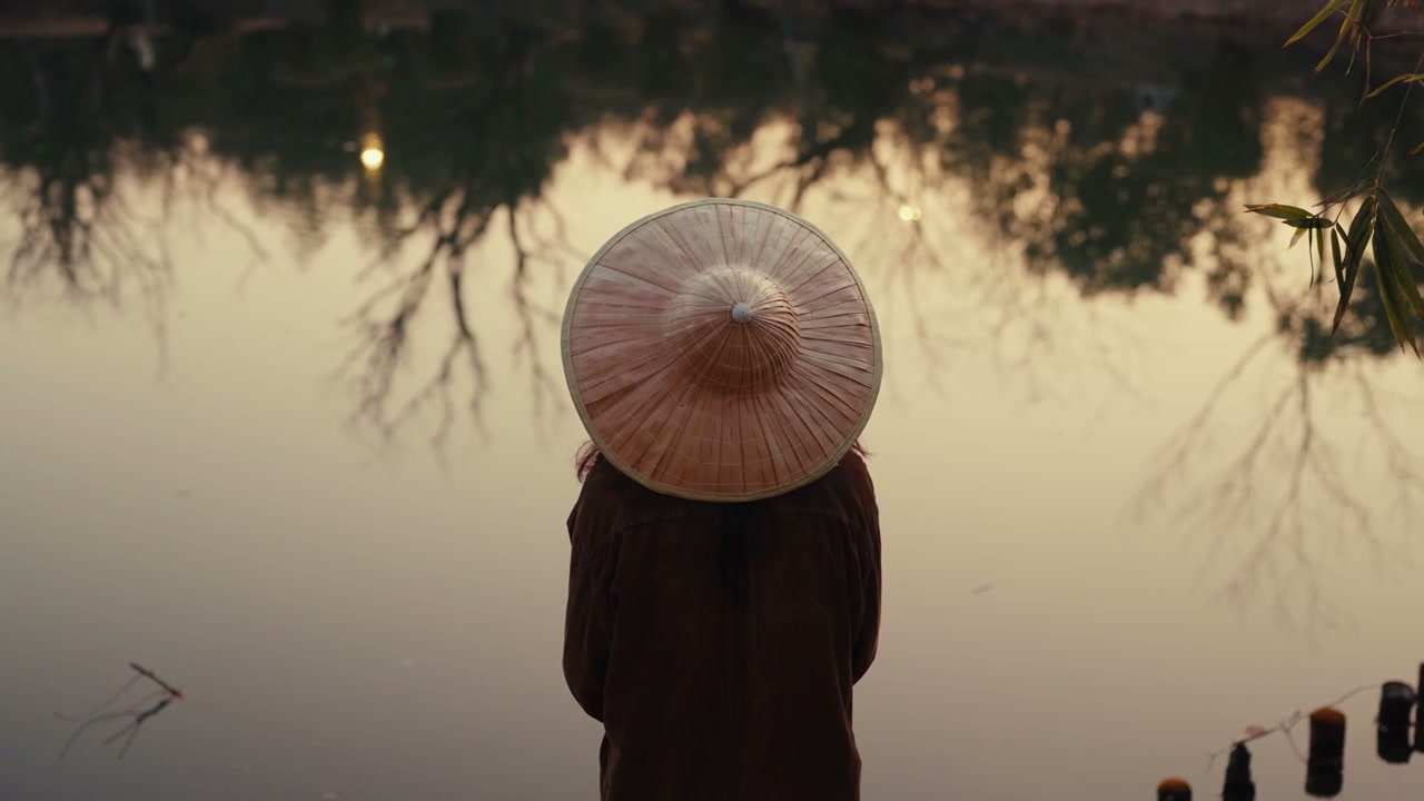 Person in Conical Hat by Lake at Sunset