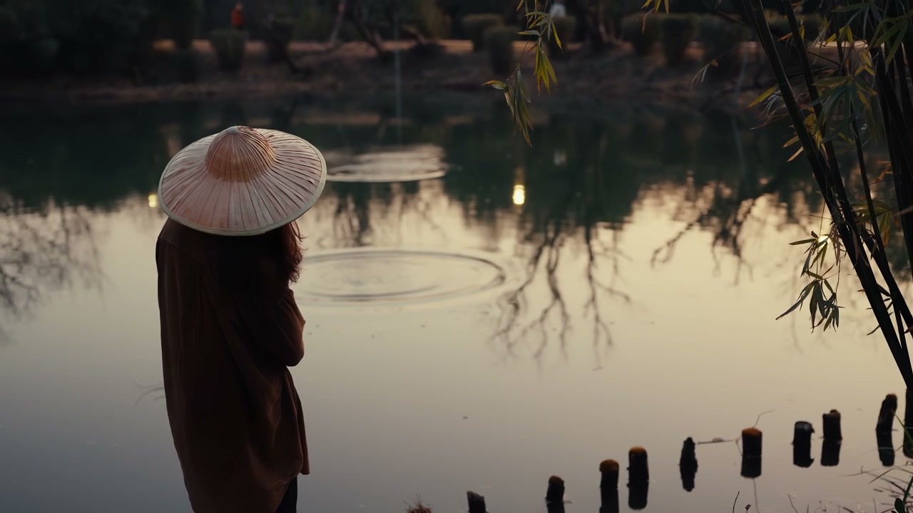 Person in Straw Hat by Tranquil Pond at Dusk