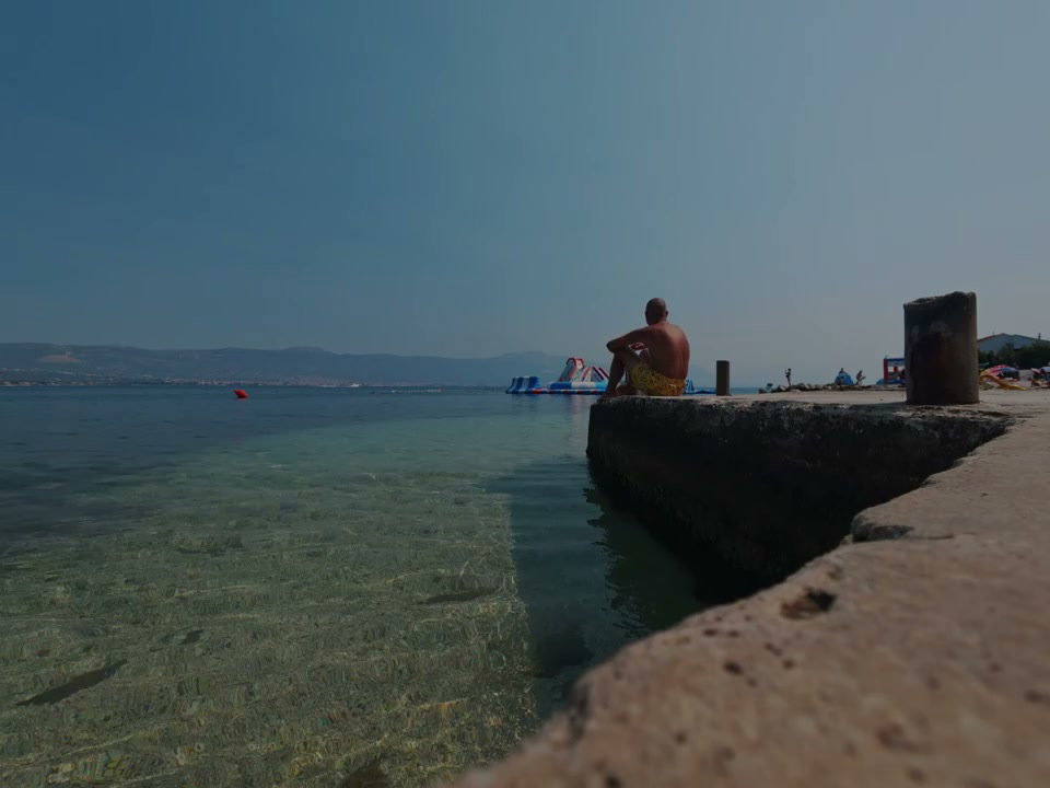 Person Sitting on Stone Pier by Clear Sea