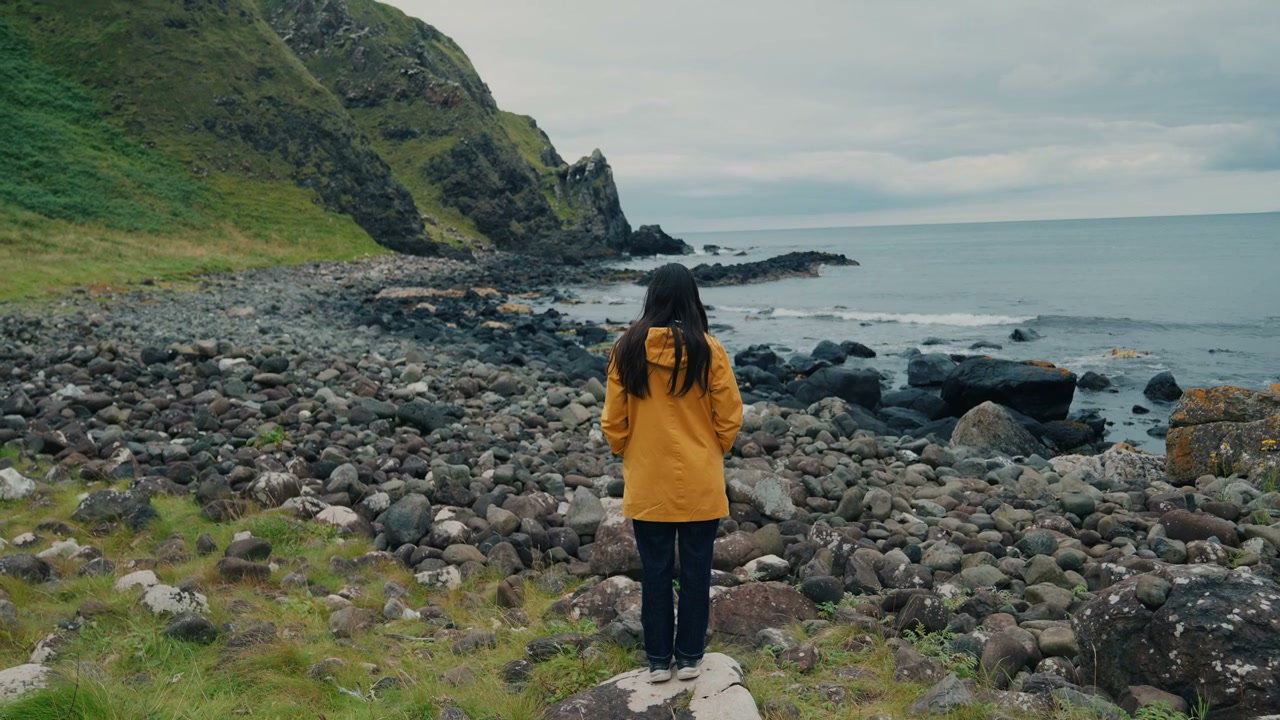 Woman in Raincoat on Rocky Coast