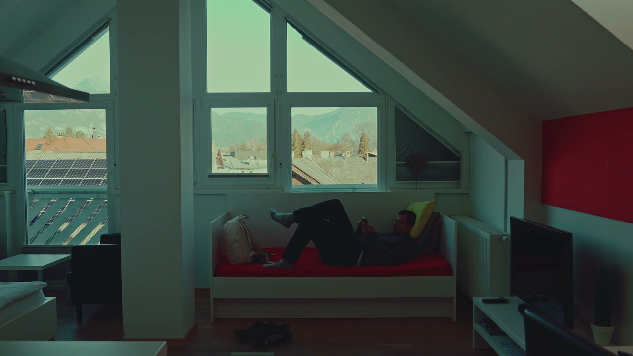 Man Using Phone on Bed in Attic with Mountain View