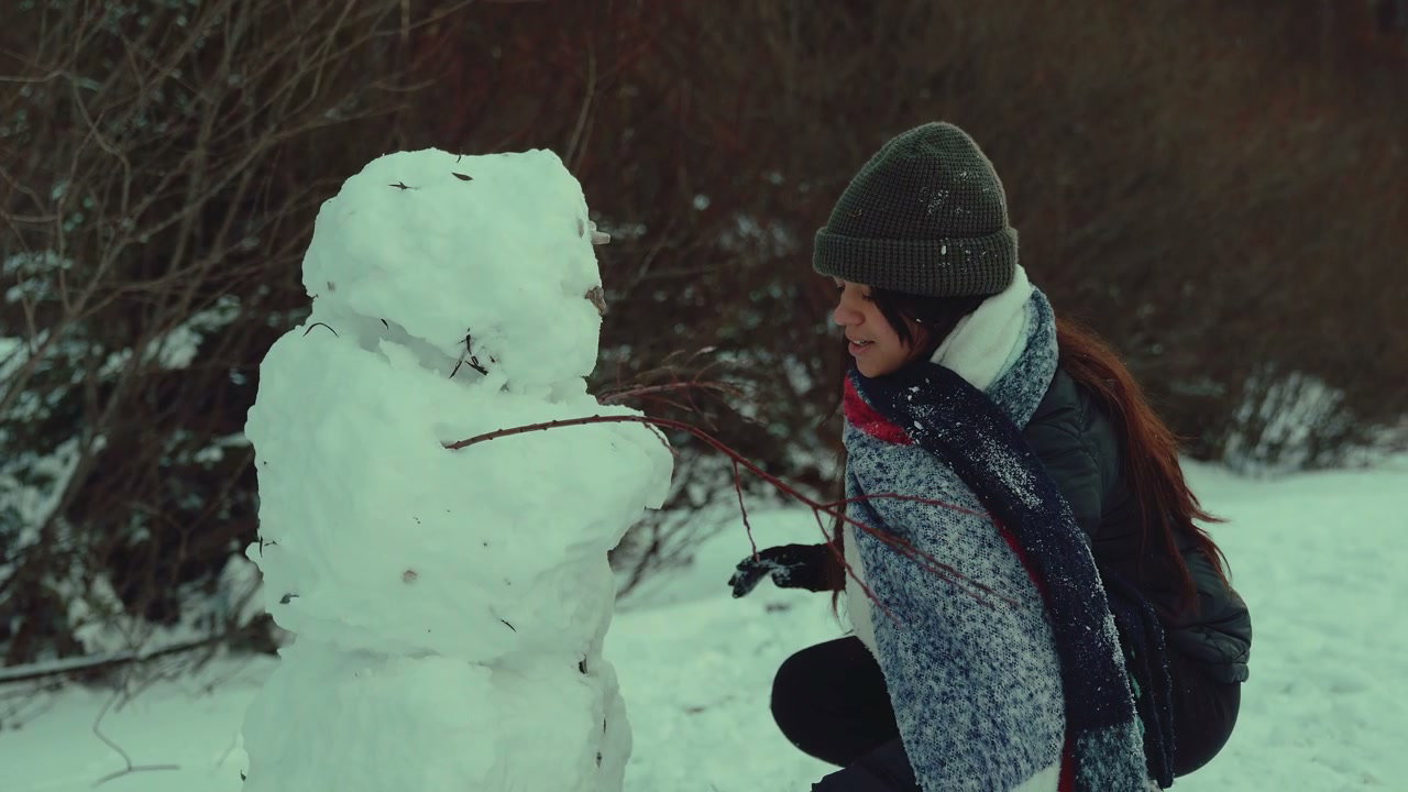 Woman Building Snowman in Snowy Park