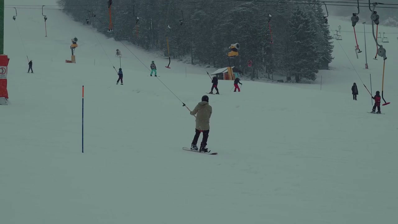 Snowboarder Using T-Bar Lift on Snowy Slope