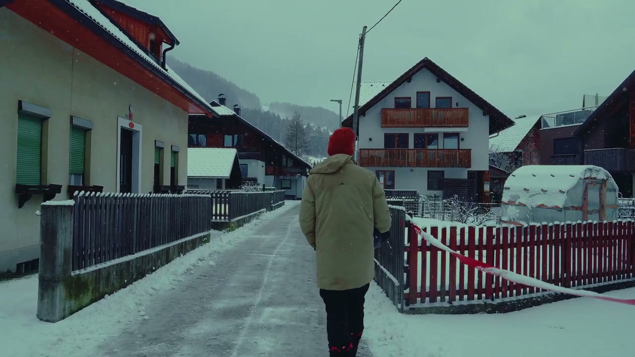 Person Walking Through Snowy Village as Snow Falls