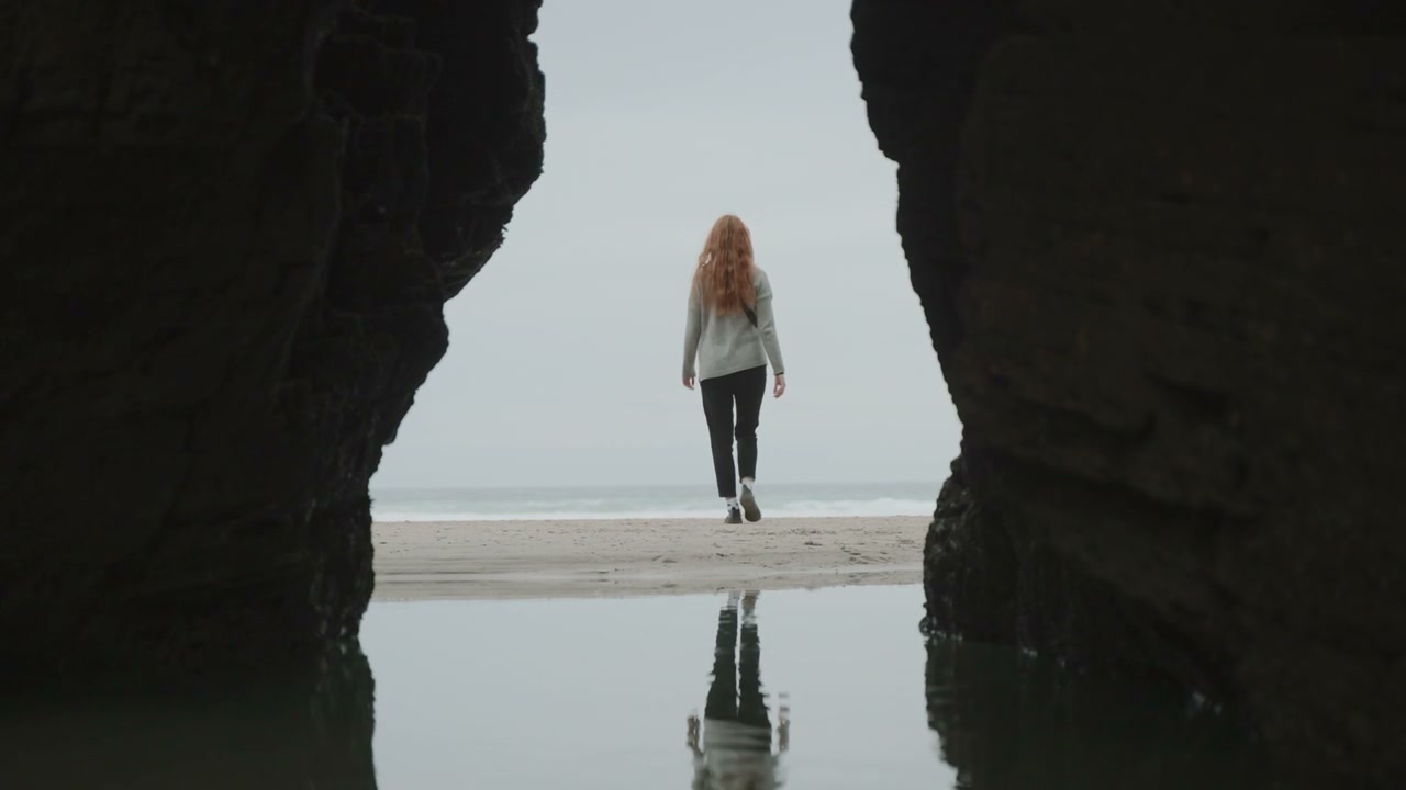 Person Walking on Coastal Beach Between Rocks