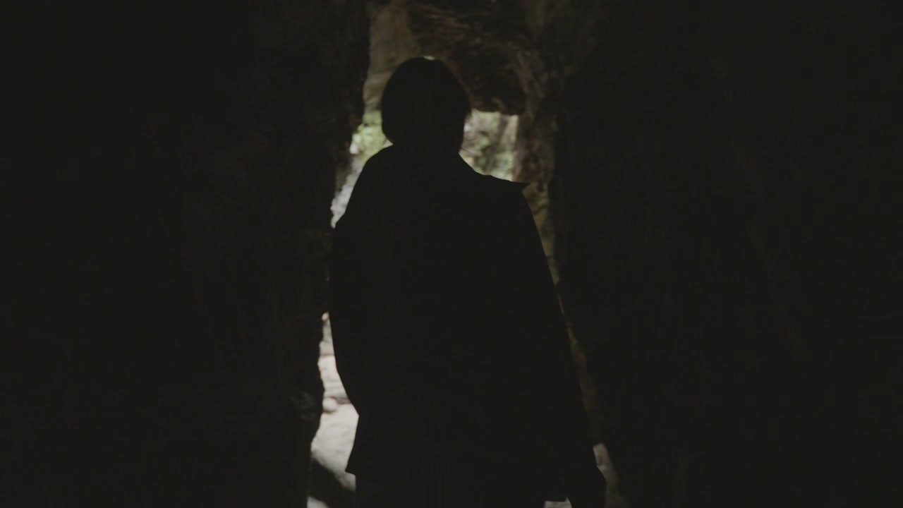 Hiker Exiting Dark Cave into Rocky Gorge