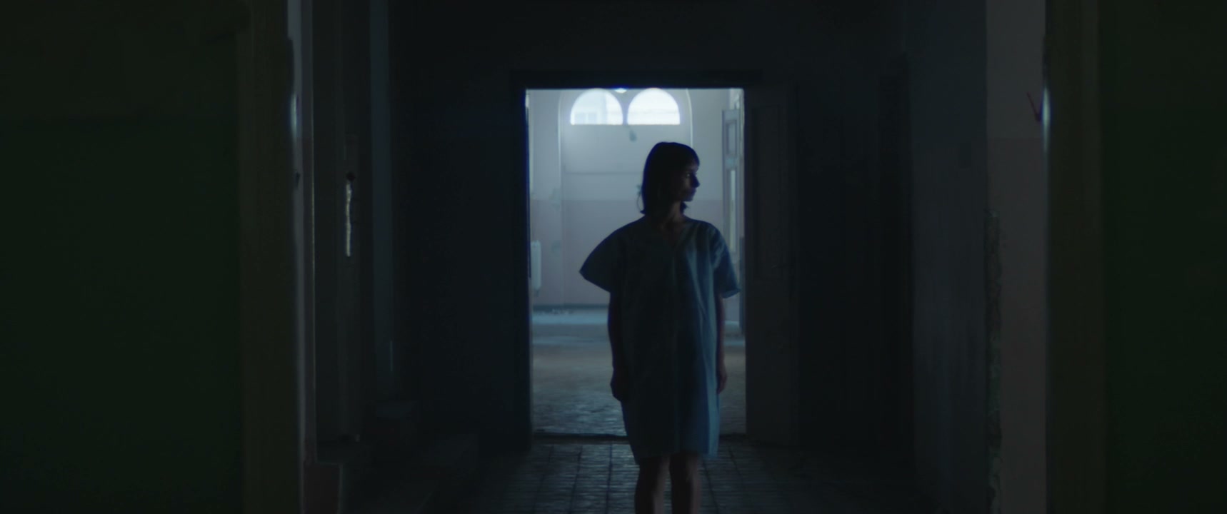 Person in Hospital Gown in Dark Corridor