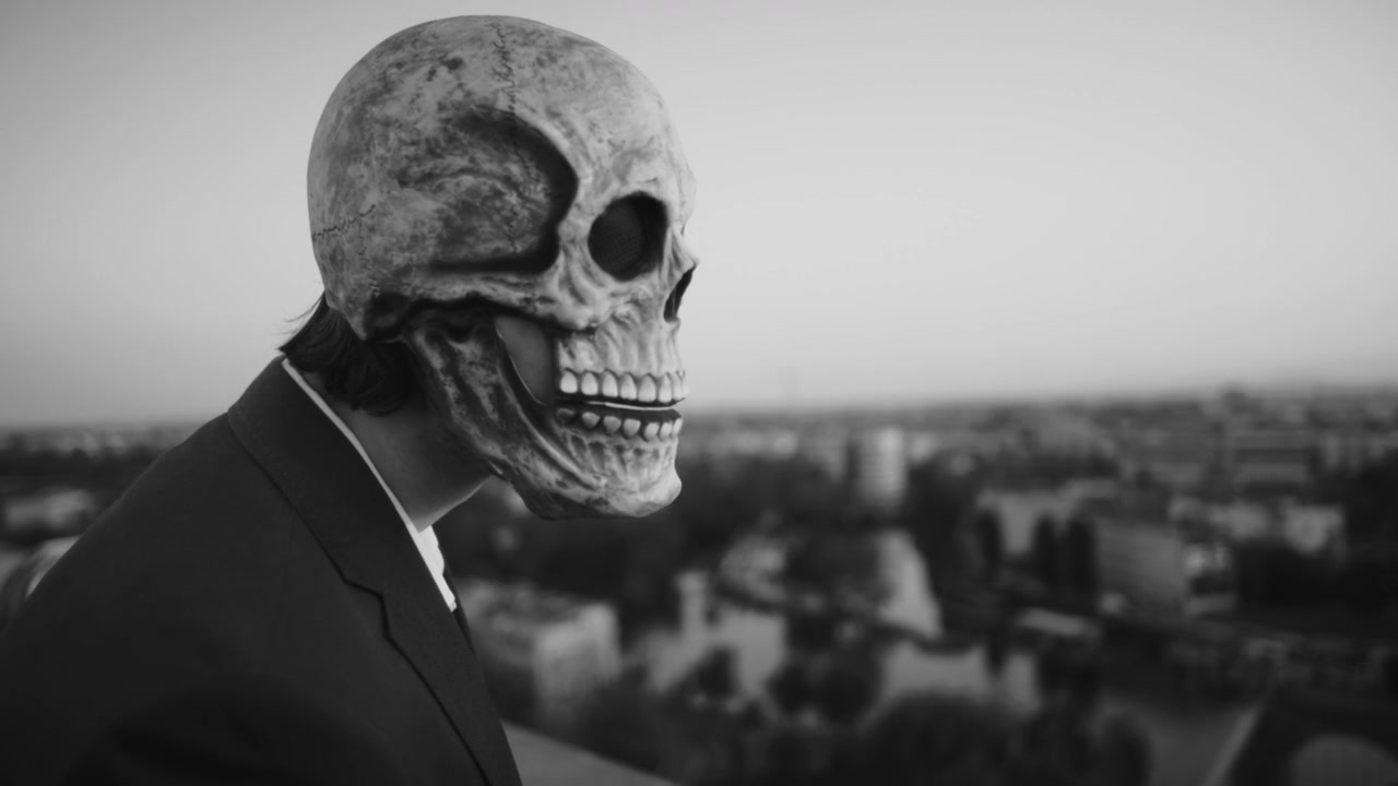Man in Skull Mask Talking on City Rooftop