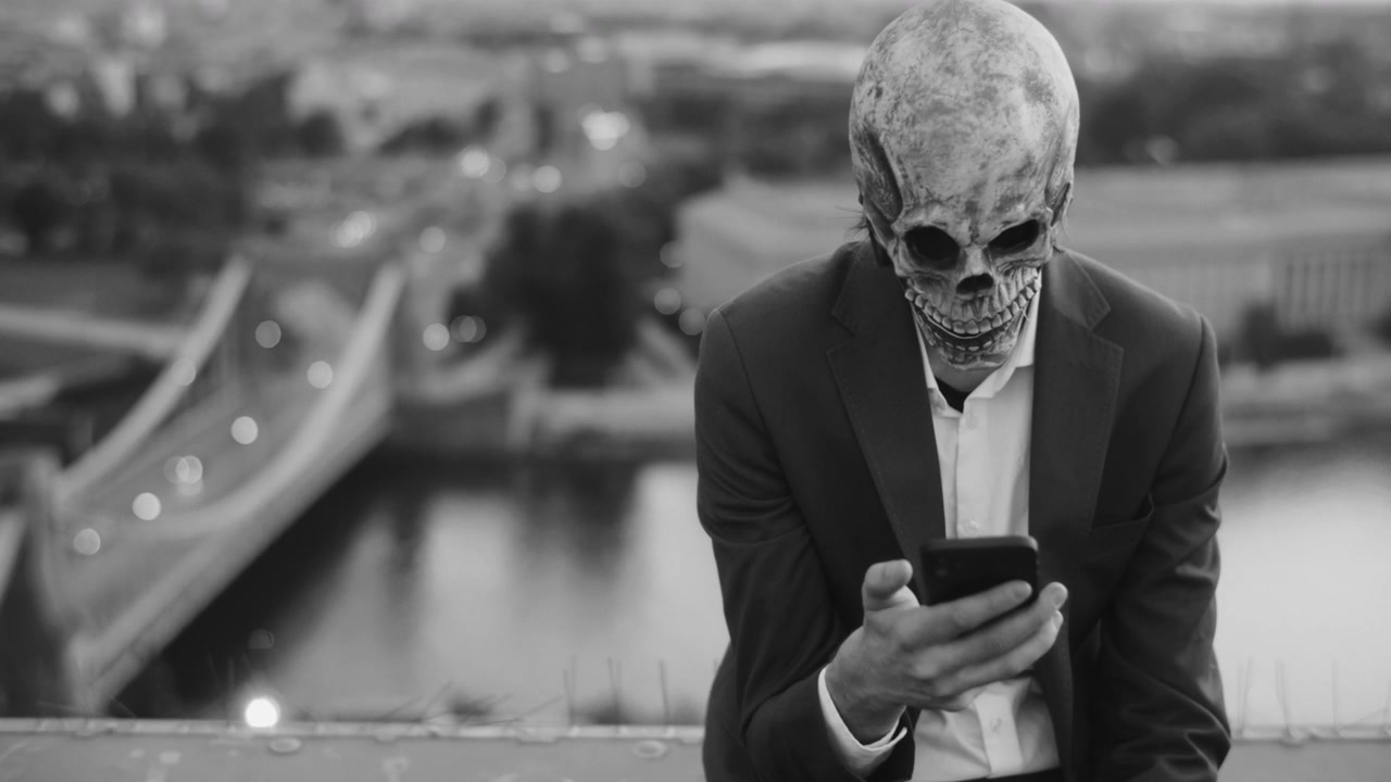 Person in Skeleton Mask Using Phone on City Rooftop