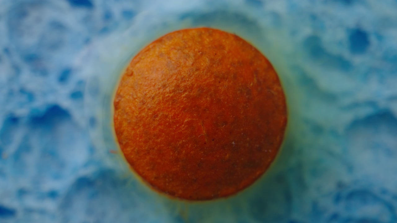 Orange Pill Dissolving in Blue Liquid