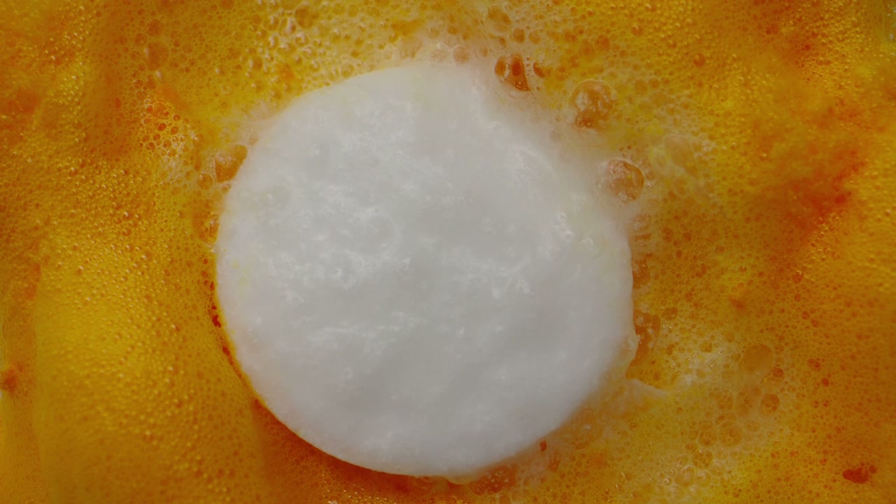 White Pill Dissolving in Orange Liquid