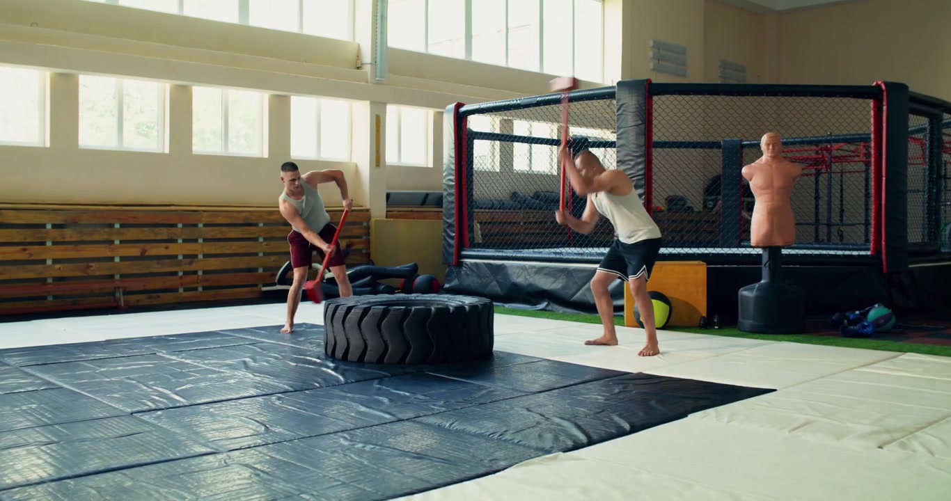 Two Men Hitting Tire with Sledgehammers in Gym